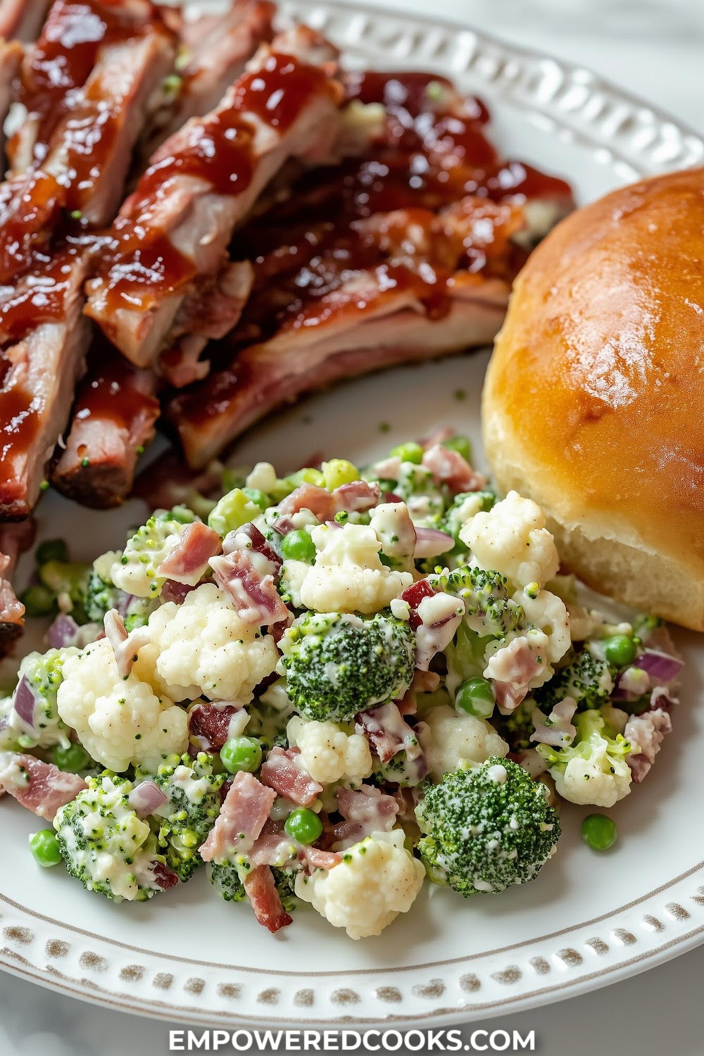 a plate of ribs with a side of a roll and broccoli pea salad