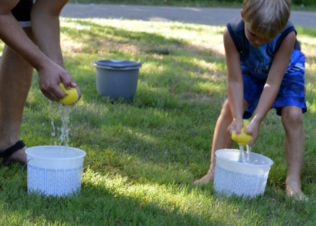 Adult and kid filling up buckets with water from sponges