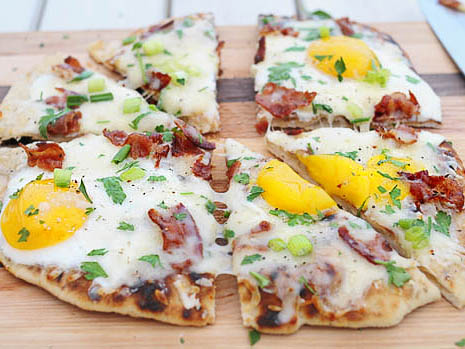 Sliced pizza with eggs, cheese, chives, and bacon