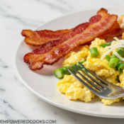 a plate of scrambled eggs with asparagus with a side of toast and bacon