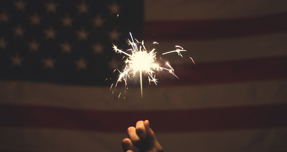 Person holding a sparkler in front of an American flag