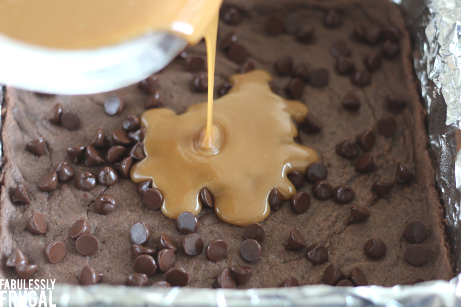 Pouring caramel over brownie chocolate chip layer