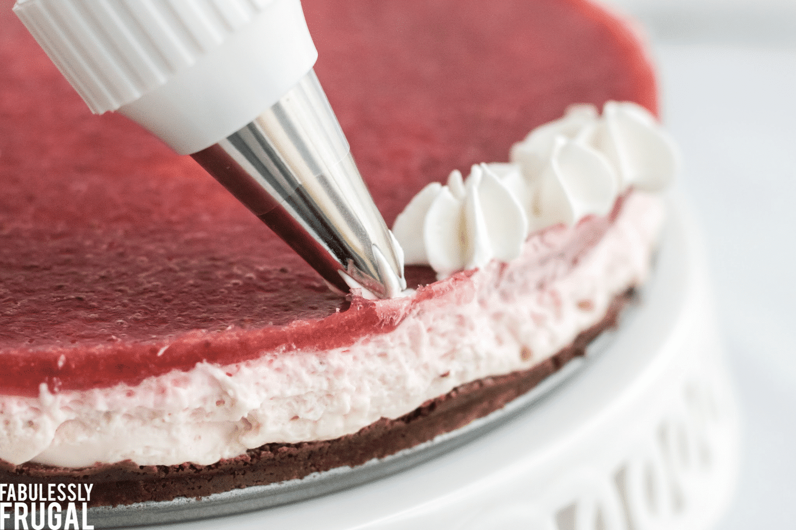 Adding whipped cream to edge of strawberry cheesecake