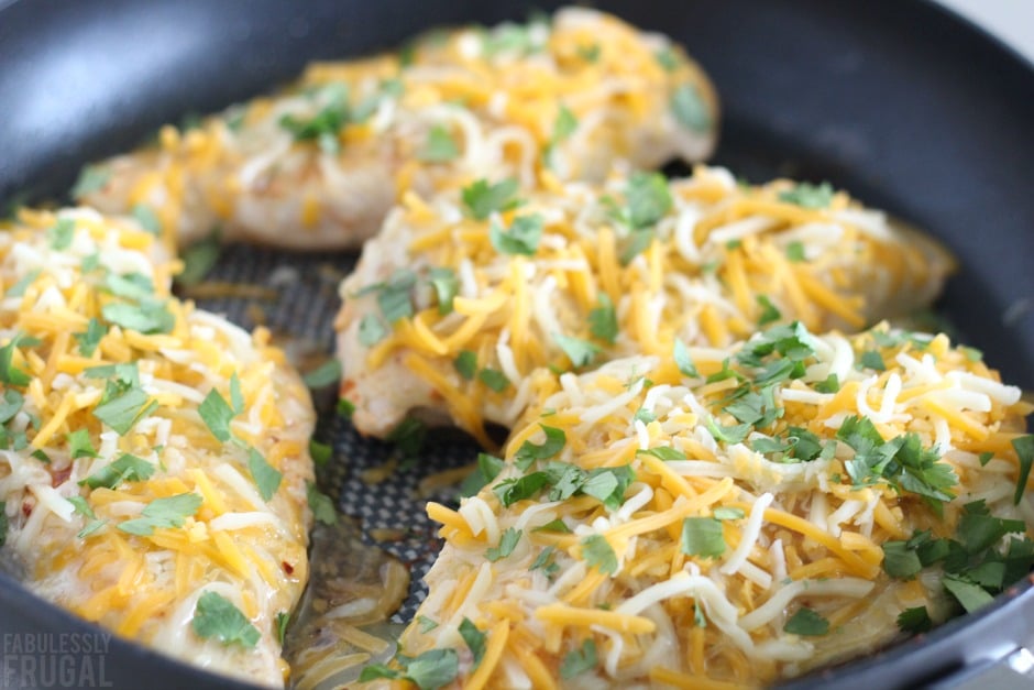 Cooking enchilada chicken breasts in skillet with cheese and toppings