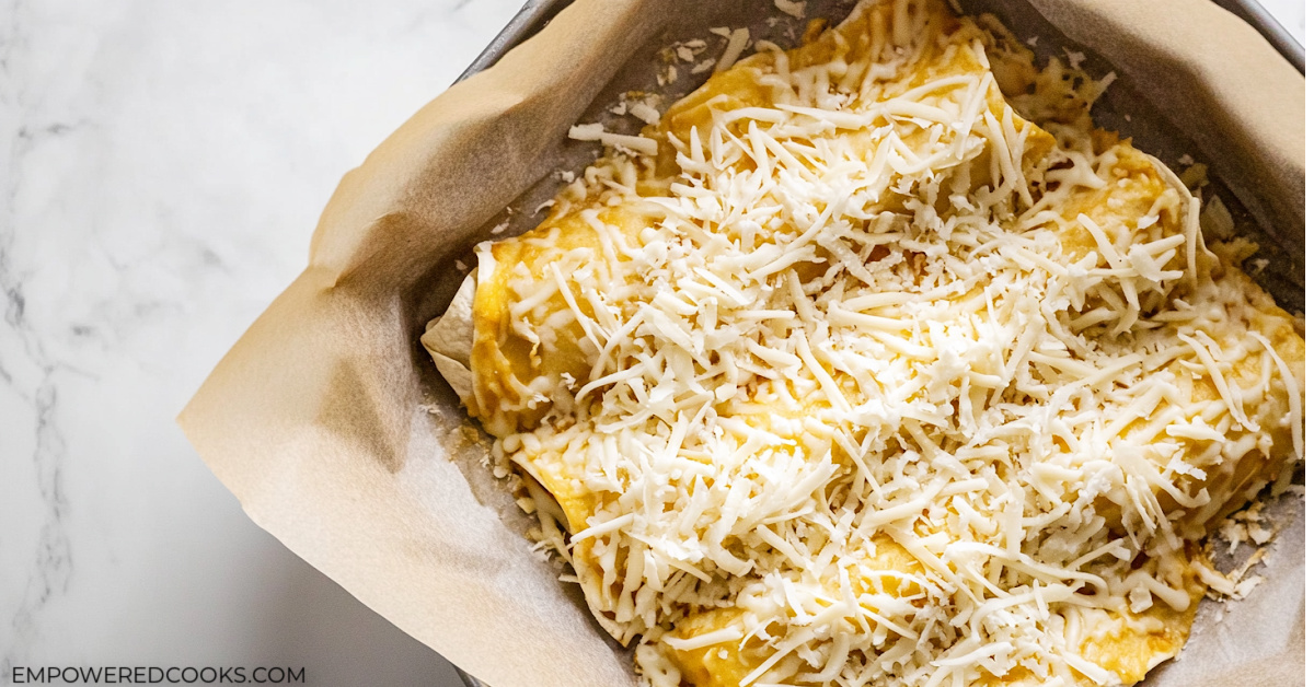 chicken enchiladas in a baking dish topped with shredded cheese