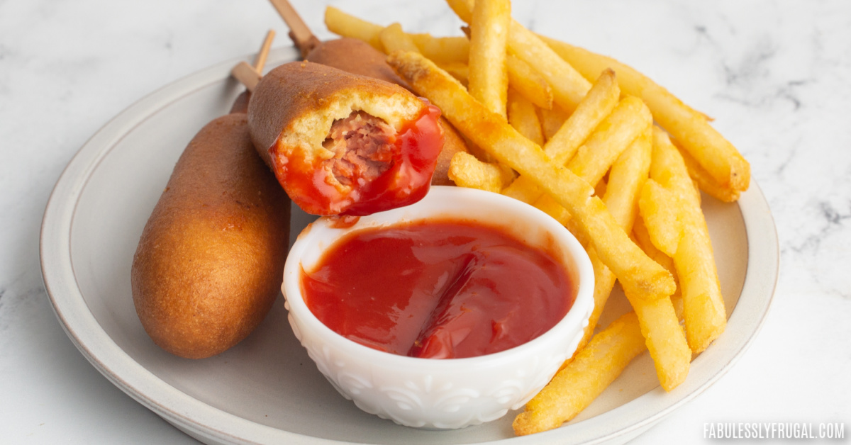 plate of fries and corn dog dipped in ketchup