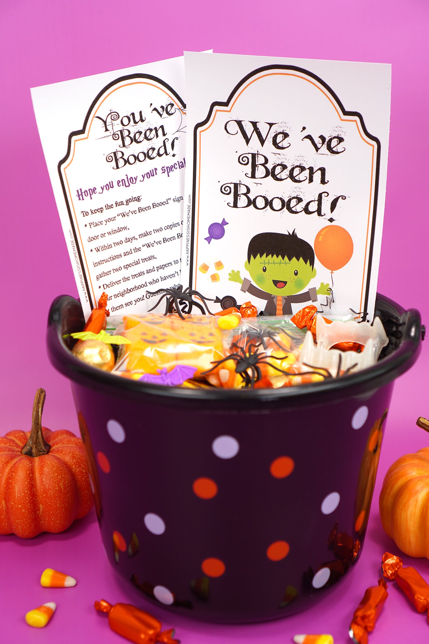 Boo Basket filled with Hallowen candy and novelty toys with "You've Been Booed"and " We've Been Booed" printable signs on purple background with pumpkins and candy corn